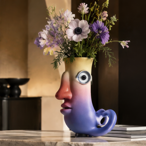 Abstract face vase with gradient glaze displayed on marble table with wild purple and white flowers — full lifestyle scene